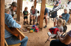 Paloma Sanchez, 3, from Austin, takes a squeezebox lesson from Terry Theis, a downtown street musician from Harper, who was playing the Kantsch. Sitting to Sanchez’ left just out of the frame is her grandmother, Francis, who was visiting from Paraguay. Strumming the guitar is Lee Haile.  In the background, Boerne resident Owen, 3, with his mother and father Gabri and Paul Burgeson, plays with a blowing horn. His grandmother, Tracy Burgeson from Colorado, to the right, claps to the beat of the music.